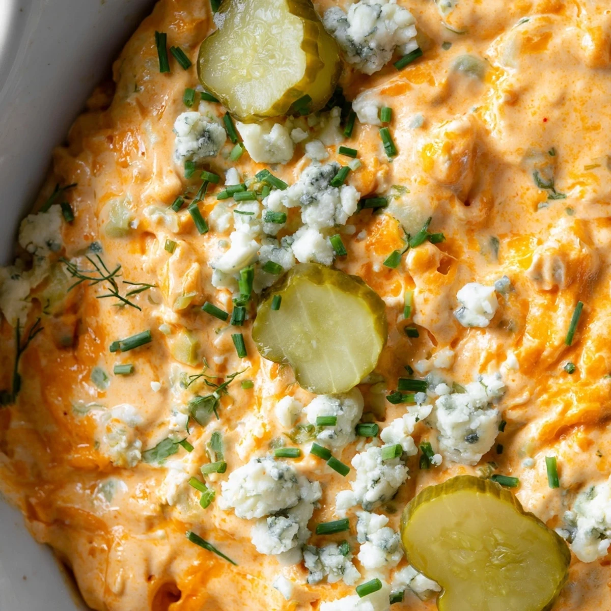Creamy buffalo pickle dip in a serving bowl surrounded by crispy chips and fresh veggie sticks
