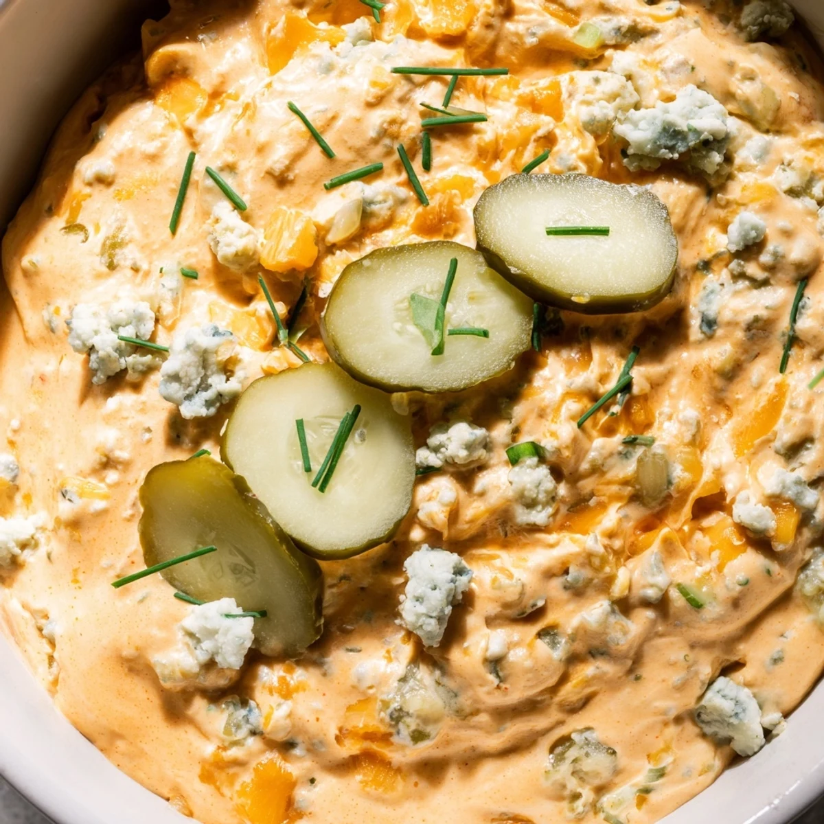 Tangy buffalo pickle dip topped with cheddar cheese and fresh chives in a rustic bowl