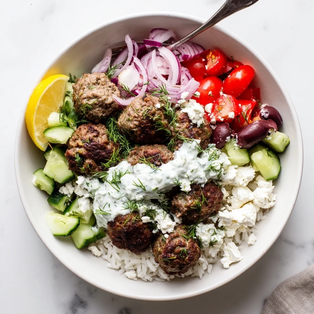 Golden brown Greek meatball bowl with feta, tomatoes, and creamy tzatziki drizzle
