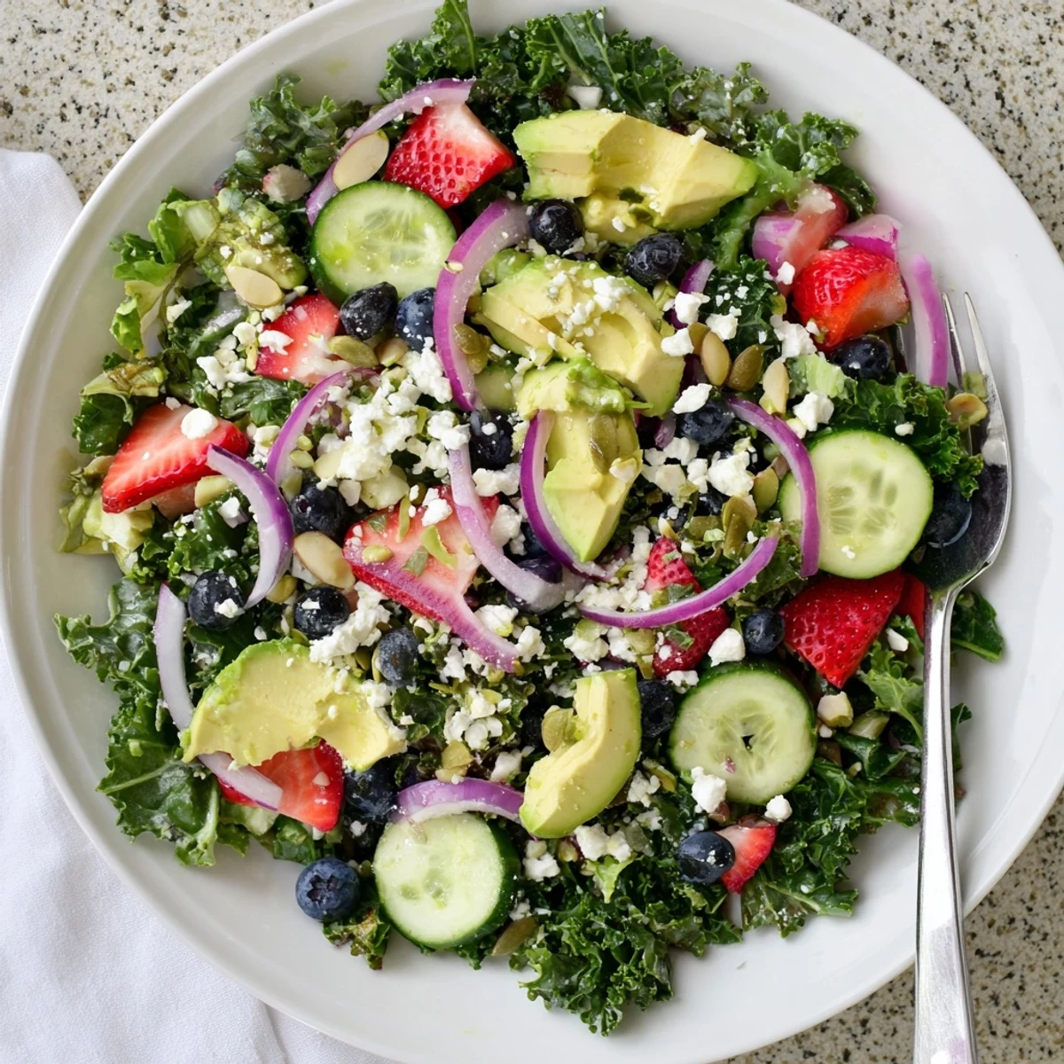 Colorful summer kale salad topped with feta, strawberries, and toasted almonds in a shallow bowl.