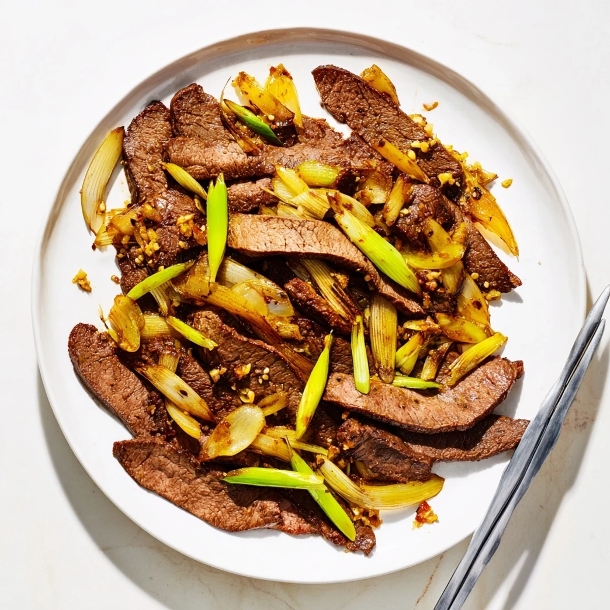 Chinese-inspired crispy beef and onion stir fry served steaming hot in a white bowl