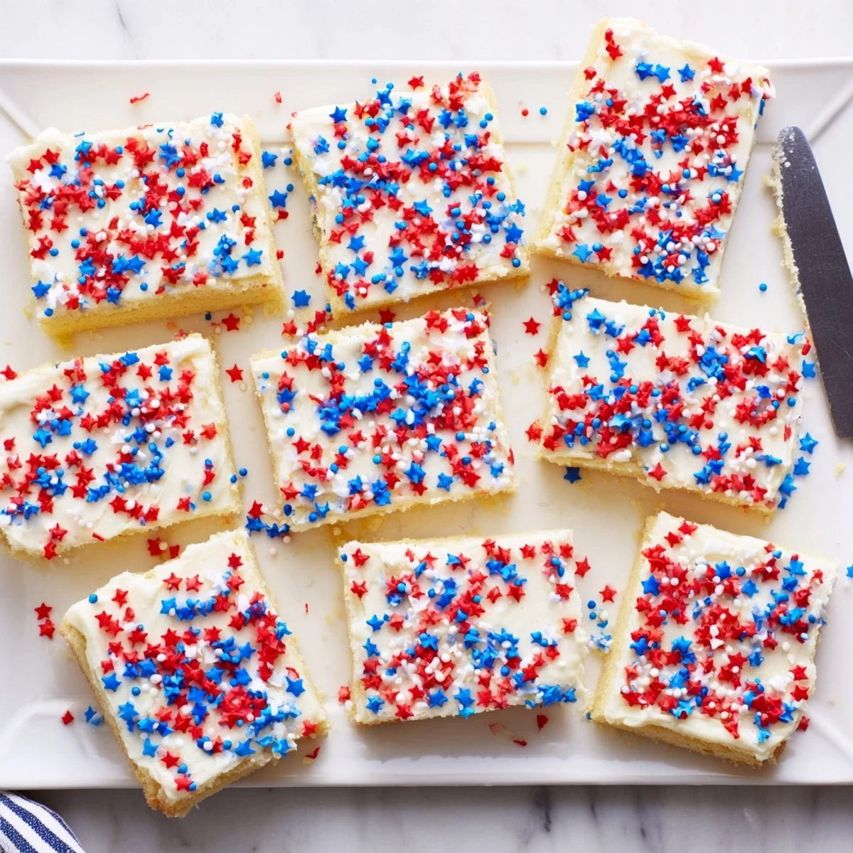 Patriotic sugar cookie bars spread with smooth white frosting and colorful festive sprinkles for Independence Day