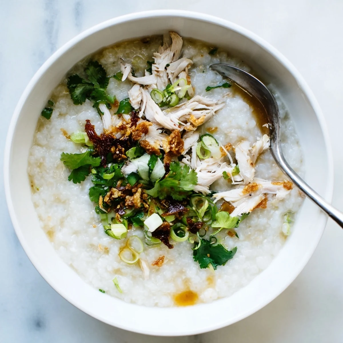 Savory chicken congee simmered in a white bowl with ginger and fried shallot garnish