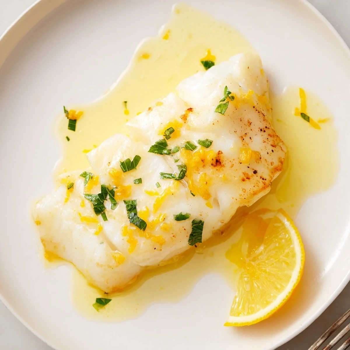 Skillet of fragrant garlic butter spooned over flaky fillets in Garlic Butter Fish Recipe.