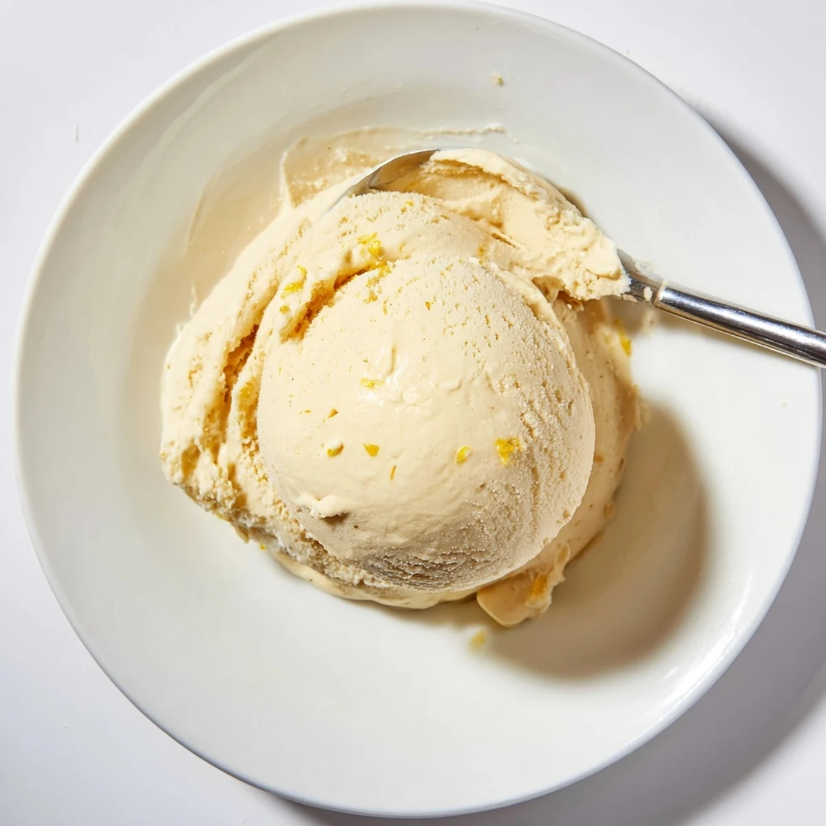 Golden scoops of dandelion honey ice cream topped with fresh yellow petals in a chilled bowl