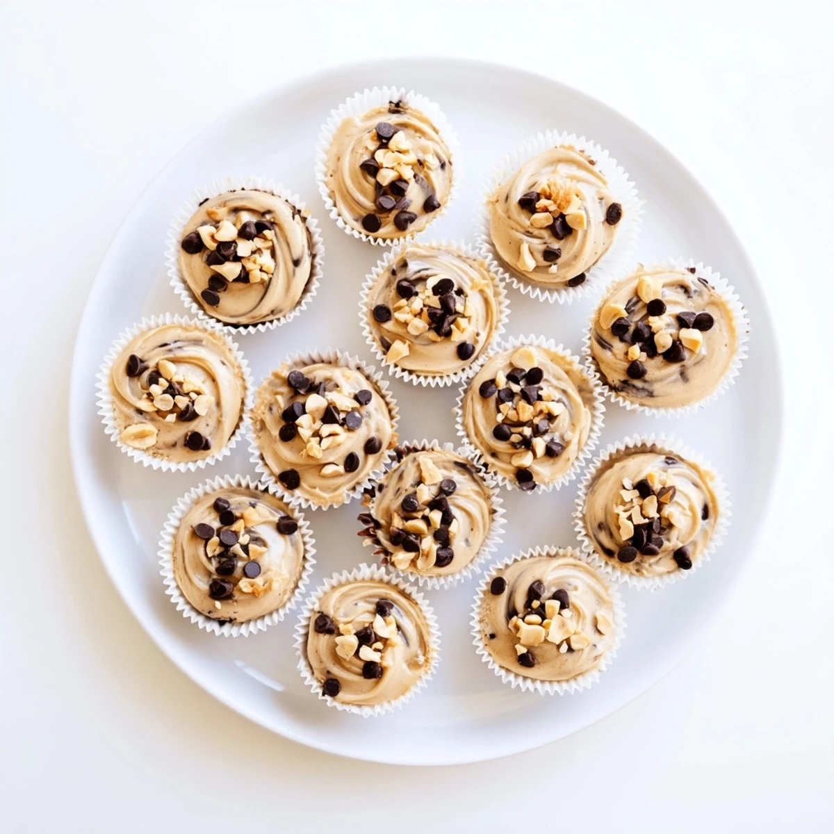 Creamy frozen peanut butter Greek yogurt bites topped with mini chocolate chips and chopped roasted peanuts in a muffin tin