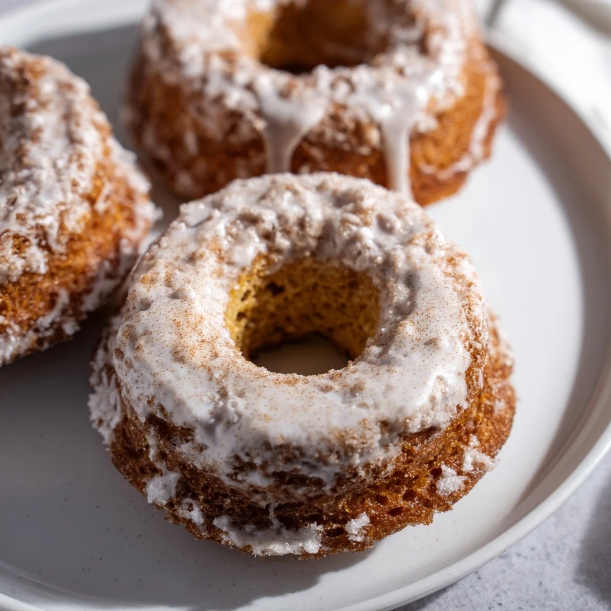 Freshly baked banana bread donuts topped with powdered sugar and ground cinnamon on a wire rack.