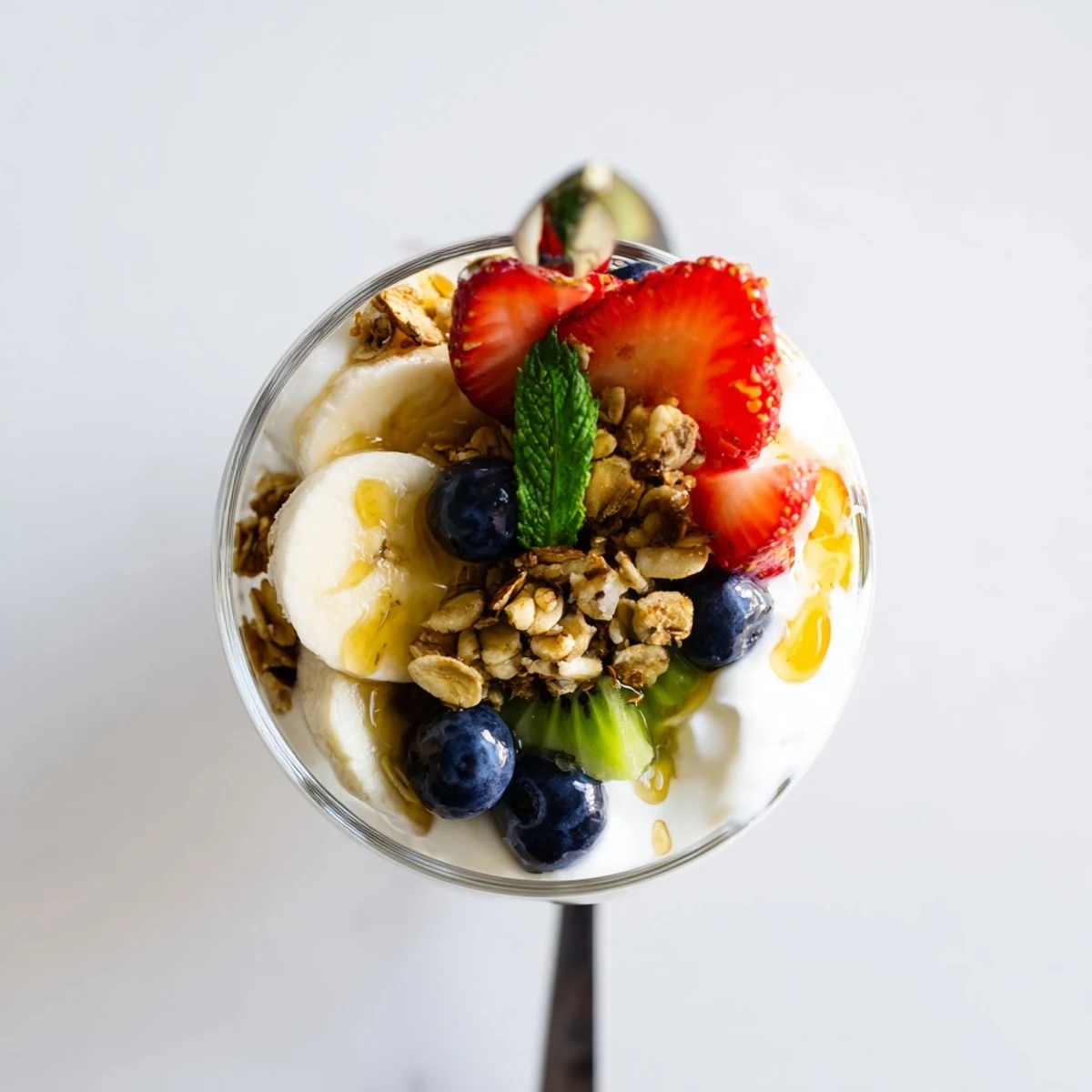 Beautiful glass parfait recipe showing yogurt honey layers with kiwi banana and mint garnish