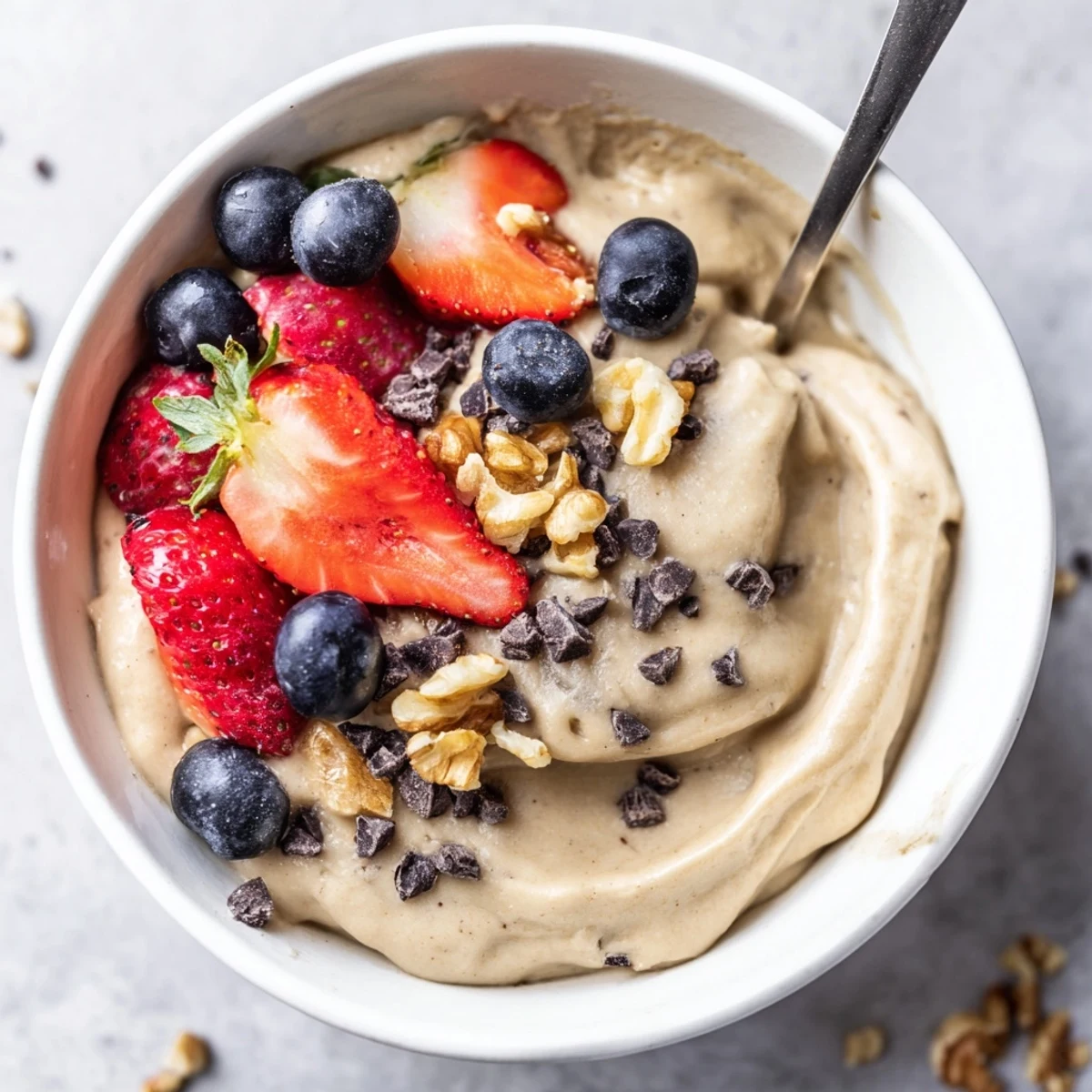 Creamy banana nice cream scooped into bowls topped with fresh berries and chopped nuts