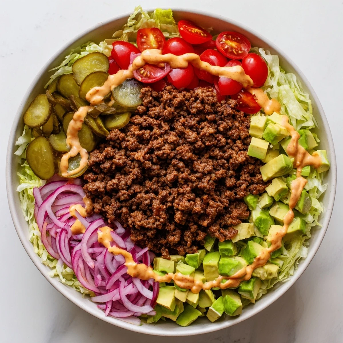 Protein-packed burger bowl featuring seasoned meat, colorful vegetables, diced avocado, and tangy sauce in a meal prep container