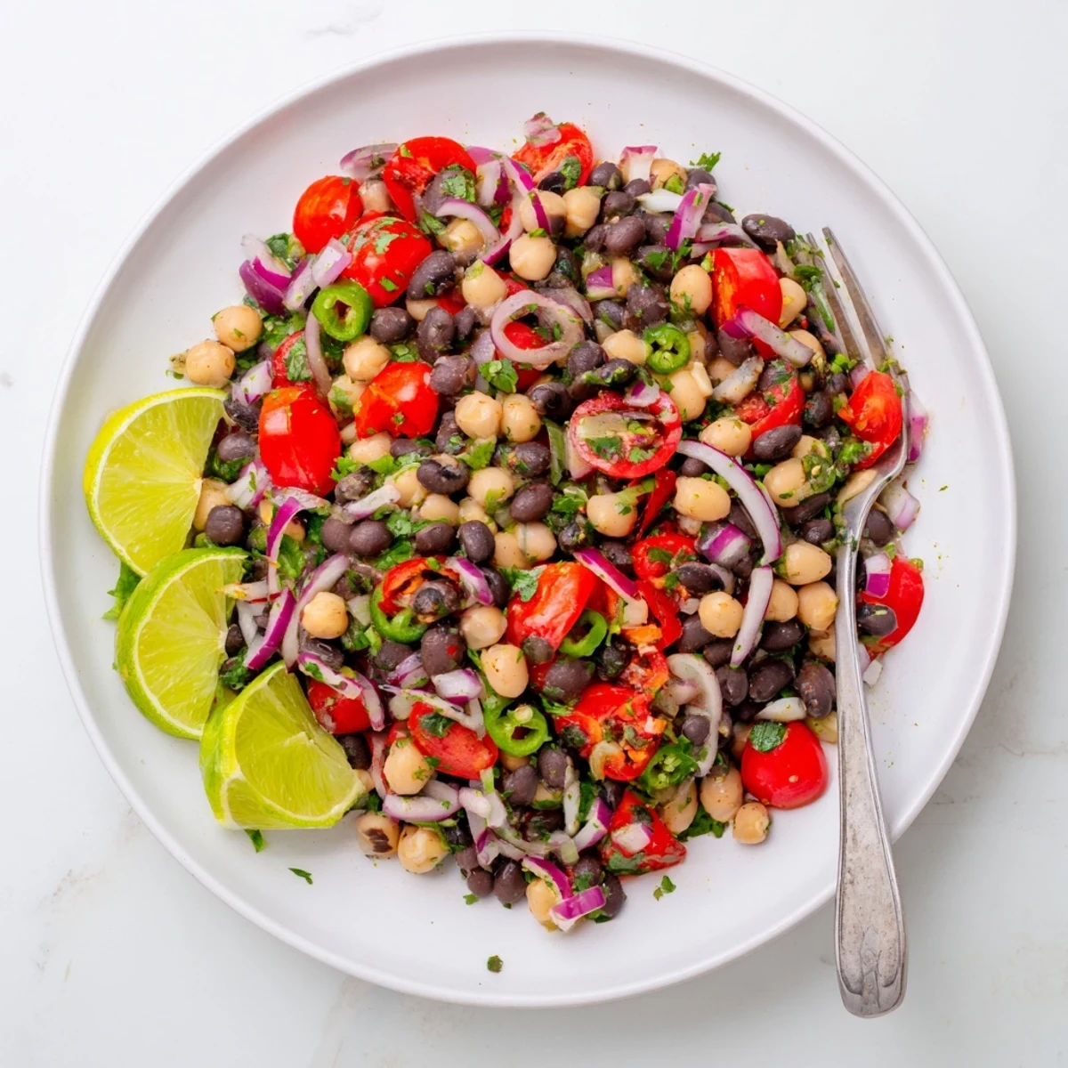Colorful marinated cilantro lime bean salad with red bell peppers and cherry tomatoes in a white bowl