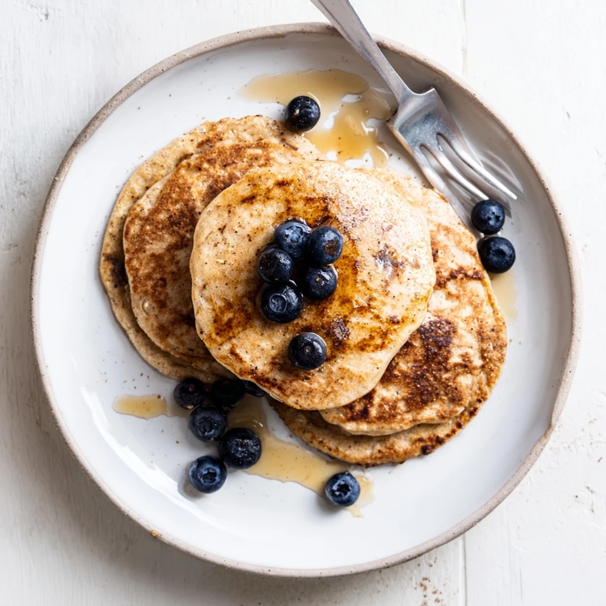 Stack of fluffy protein banana pancakes topped with fresh banana slices and maple syrup