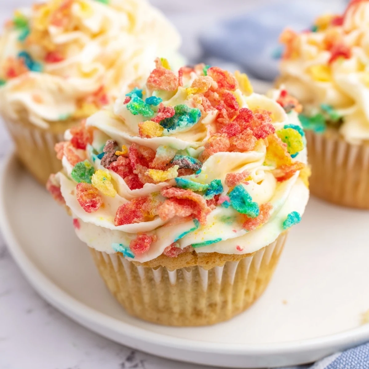 Vibrant Fruity Pebbles cereal frosting piped onto cupcakes with colorful rainbow cereal garnish