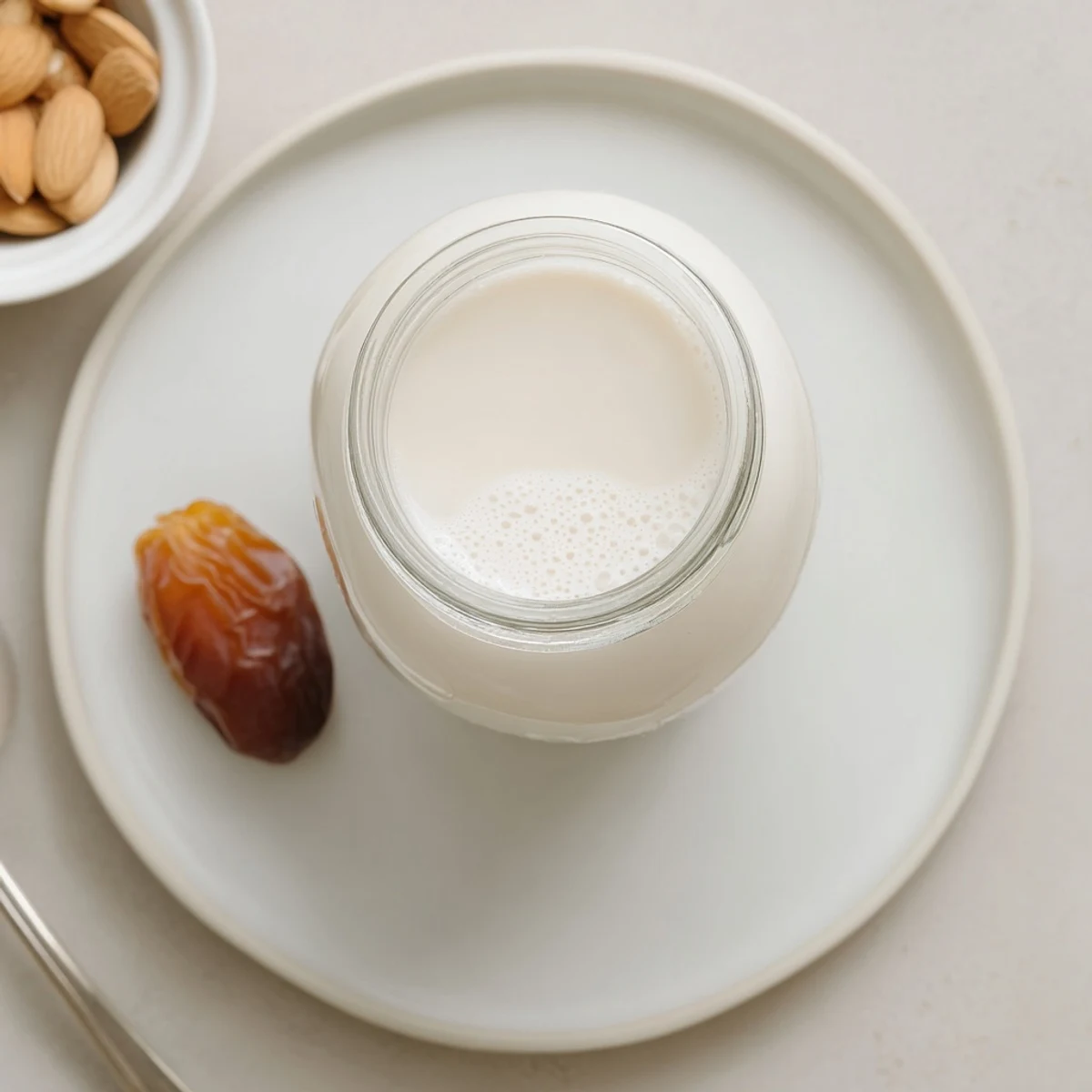 Creamy homemade Almond Milk poured into glass next to cereal bowl