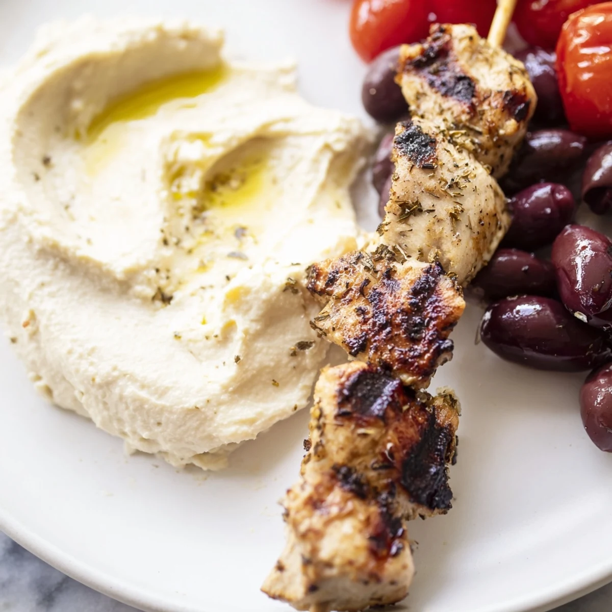 Juicy charred Greek chicken souvlaki arranged on a wooden board beside crisp cucumbers, olives, and warm pita wedges.