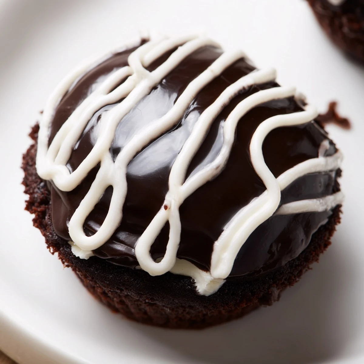 Chocolate Homemade Hostess Cupcakes topped with shiny ganache frosting and piped white icing squiggles ready to serve