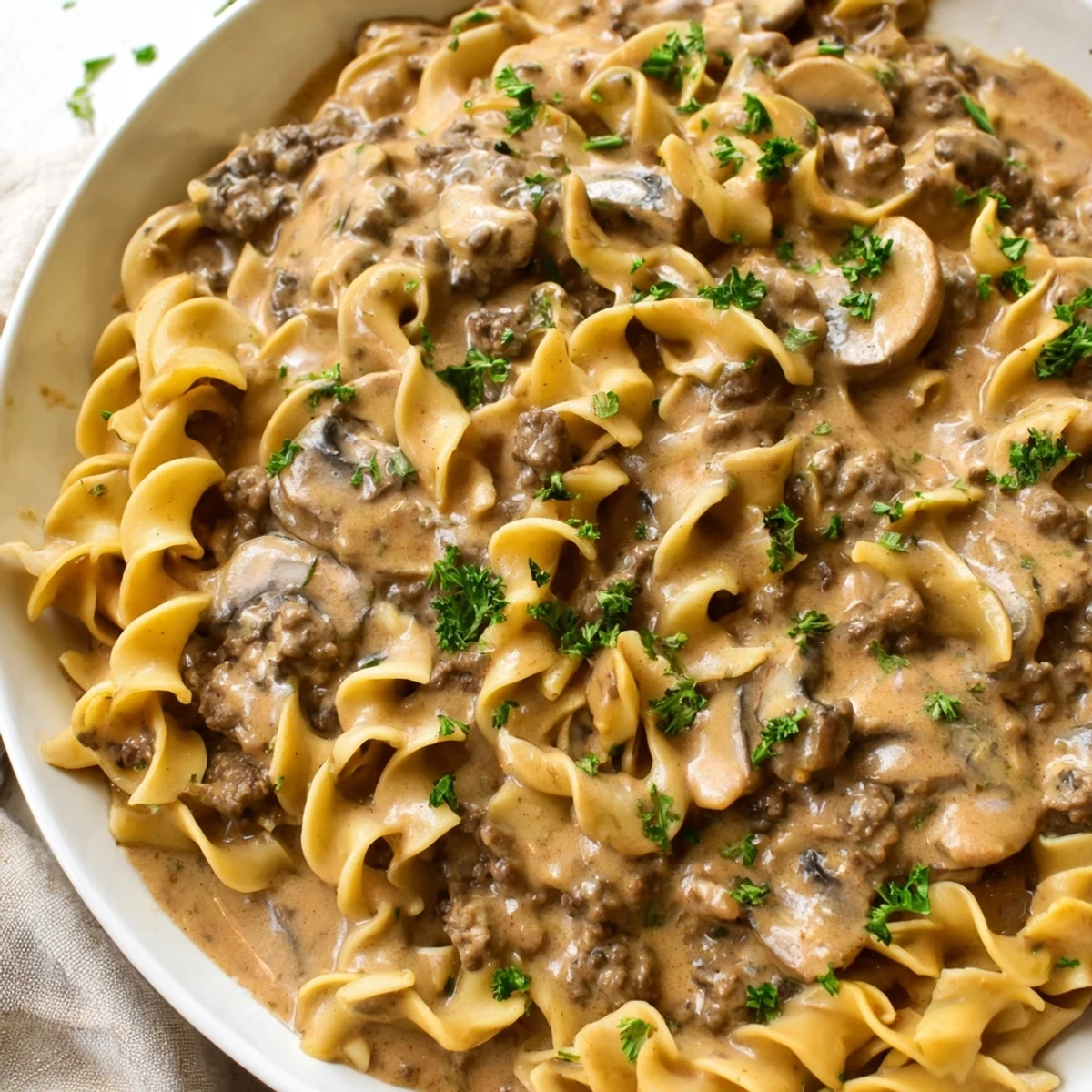 Steaming bowl of Hearty Hamburger Stroganoff topped with fresh parsley garnish