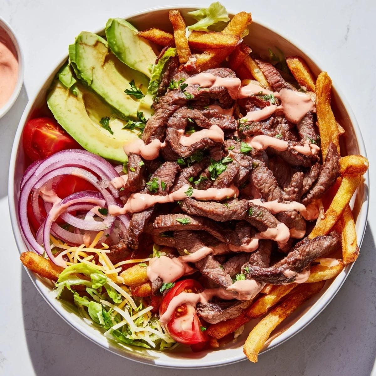 Juicy steak strips crispy fries bowl topped with avocado tomatoes and melted cheddar