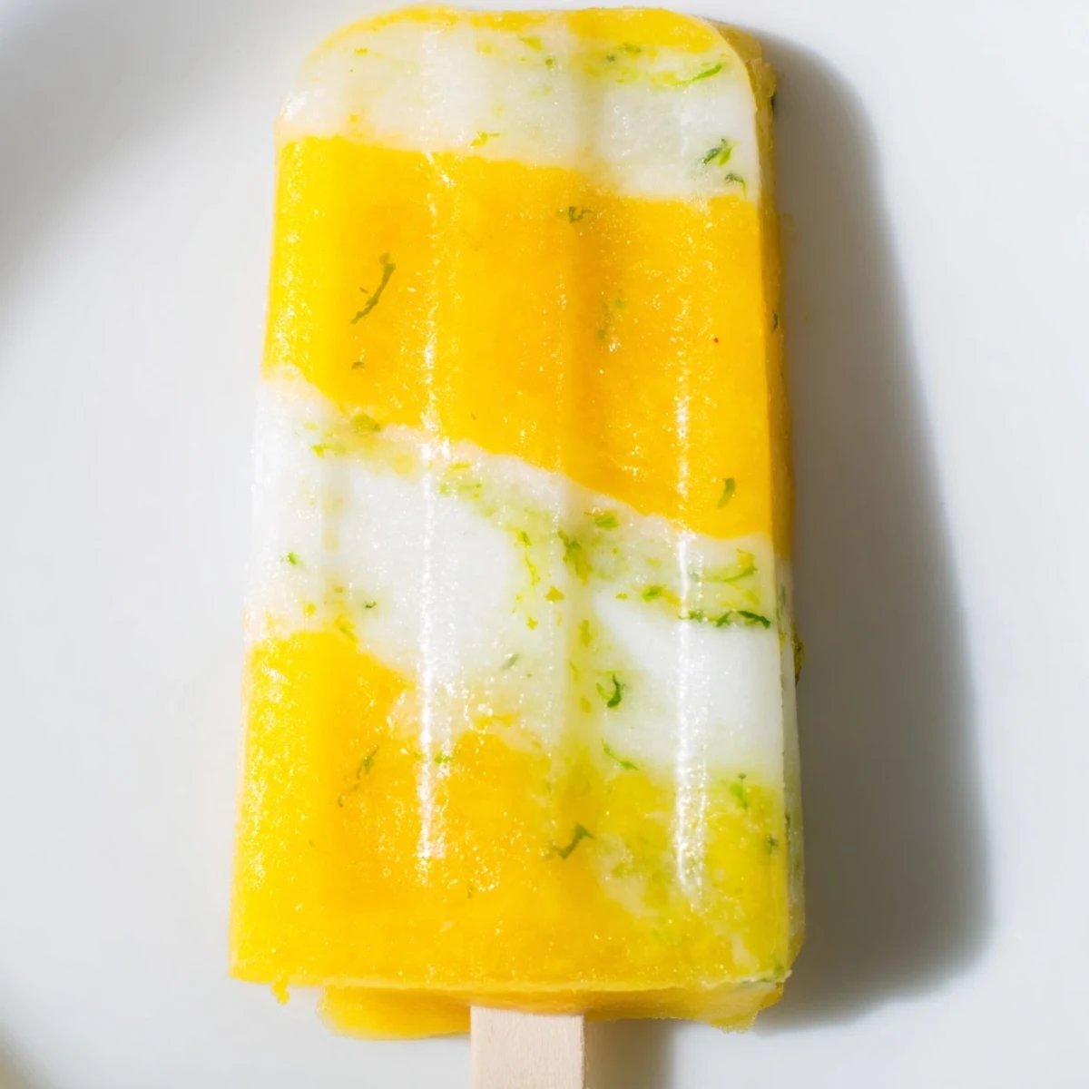 Tropical pineapple coconut lime popsicles swirl creamy layers on a wooden stick.