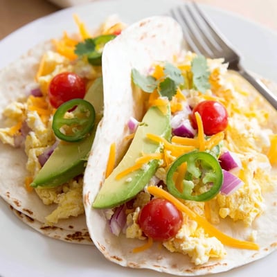 Warm breakfast tacos recipe loaded with cheese, tomatoes, and savory scrambled eggs  
